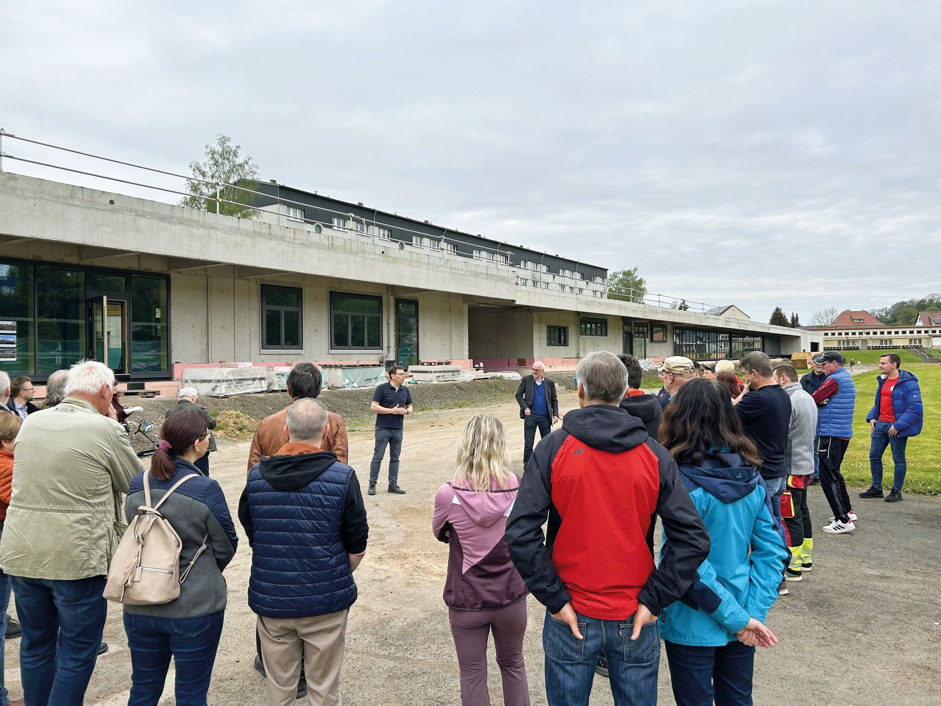 Eine Gruppe von Menschen stehen vor dem, sich noch in der Fertigstellung befindenden, Kommunikations-, Sport- und Freizeitzentrum.