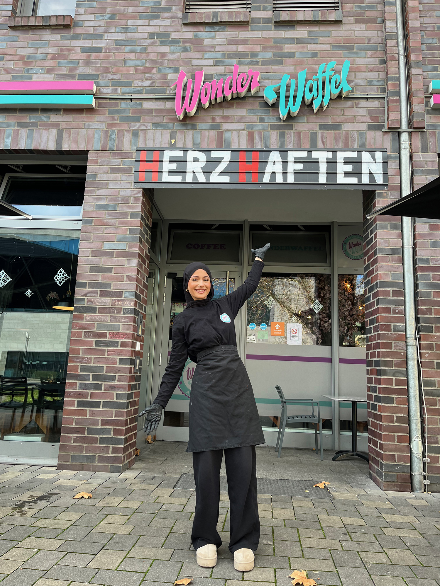Frau steht vor der Eingangstür von Wonder Waffel und streckt einen Arm in die Höhe.