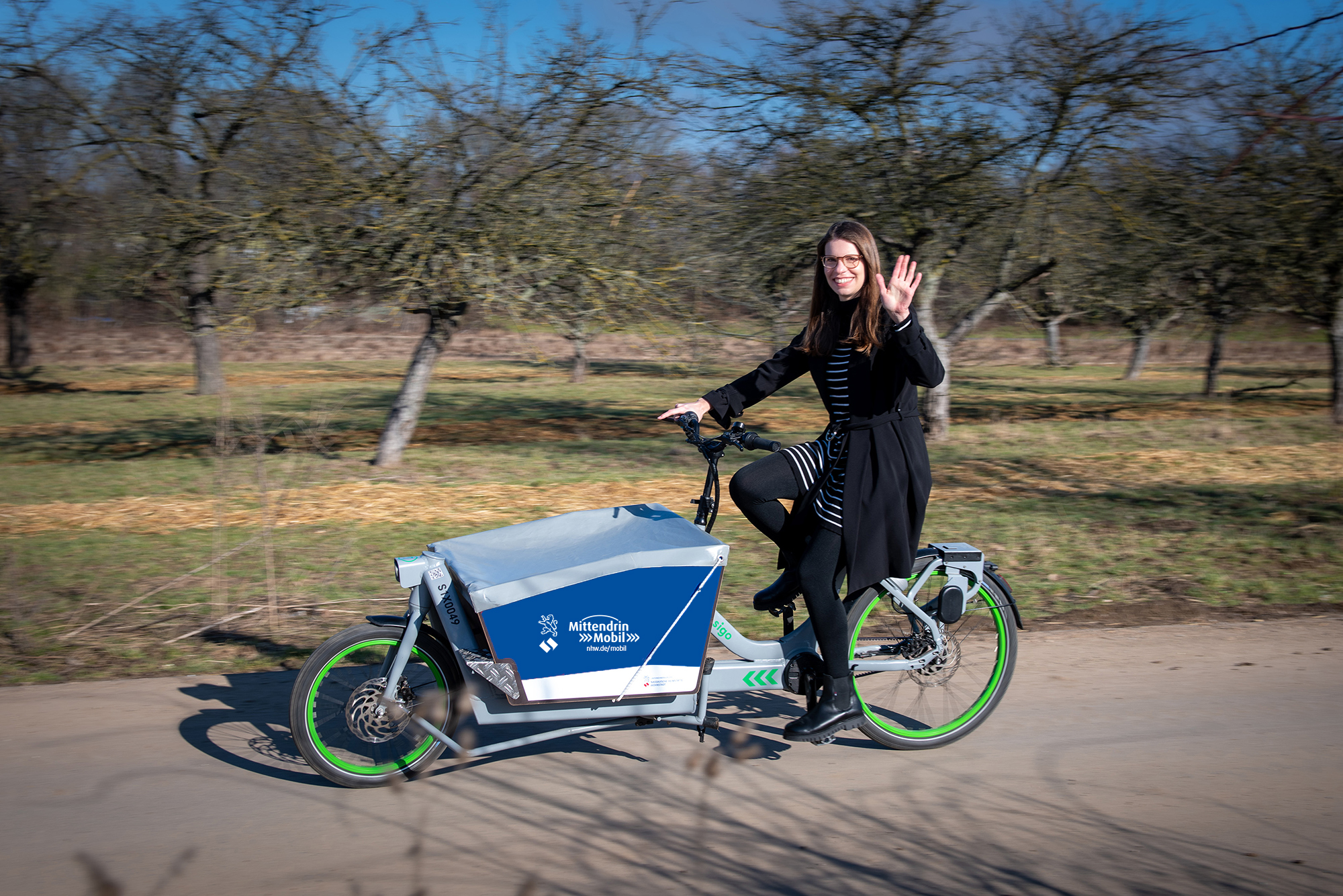 Frau fährt ein Lastenrad. Auf der Lastenradbox ist das NHW Logo und die URL nhw.de/mobil