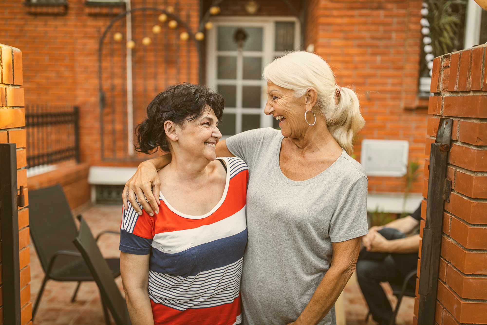 Zwei ältere Frauen halten sich seitlich im Arm und lachen sich an.
