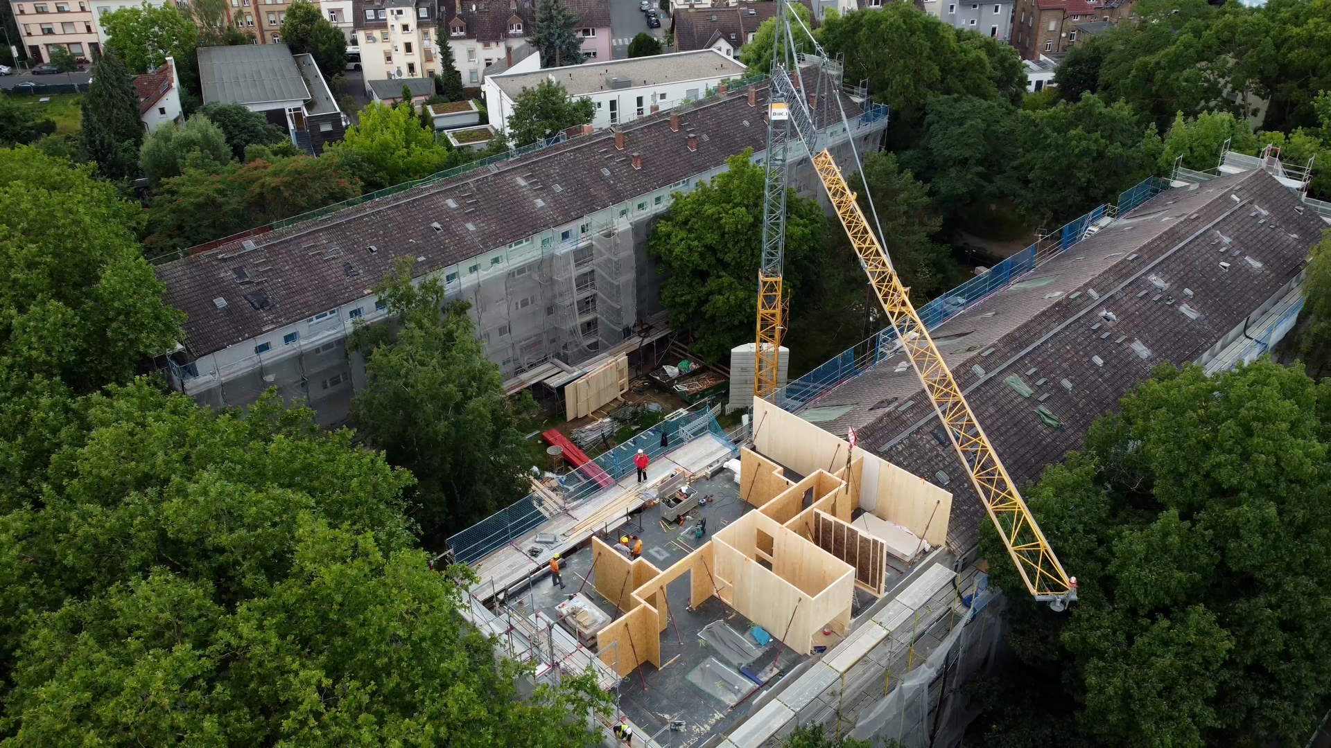 Luftaufnahme von einem Haus. Das Dach fehlt, darauf zu sehen sind Holzmodule und ein Kran.