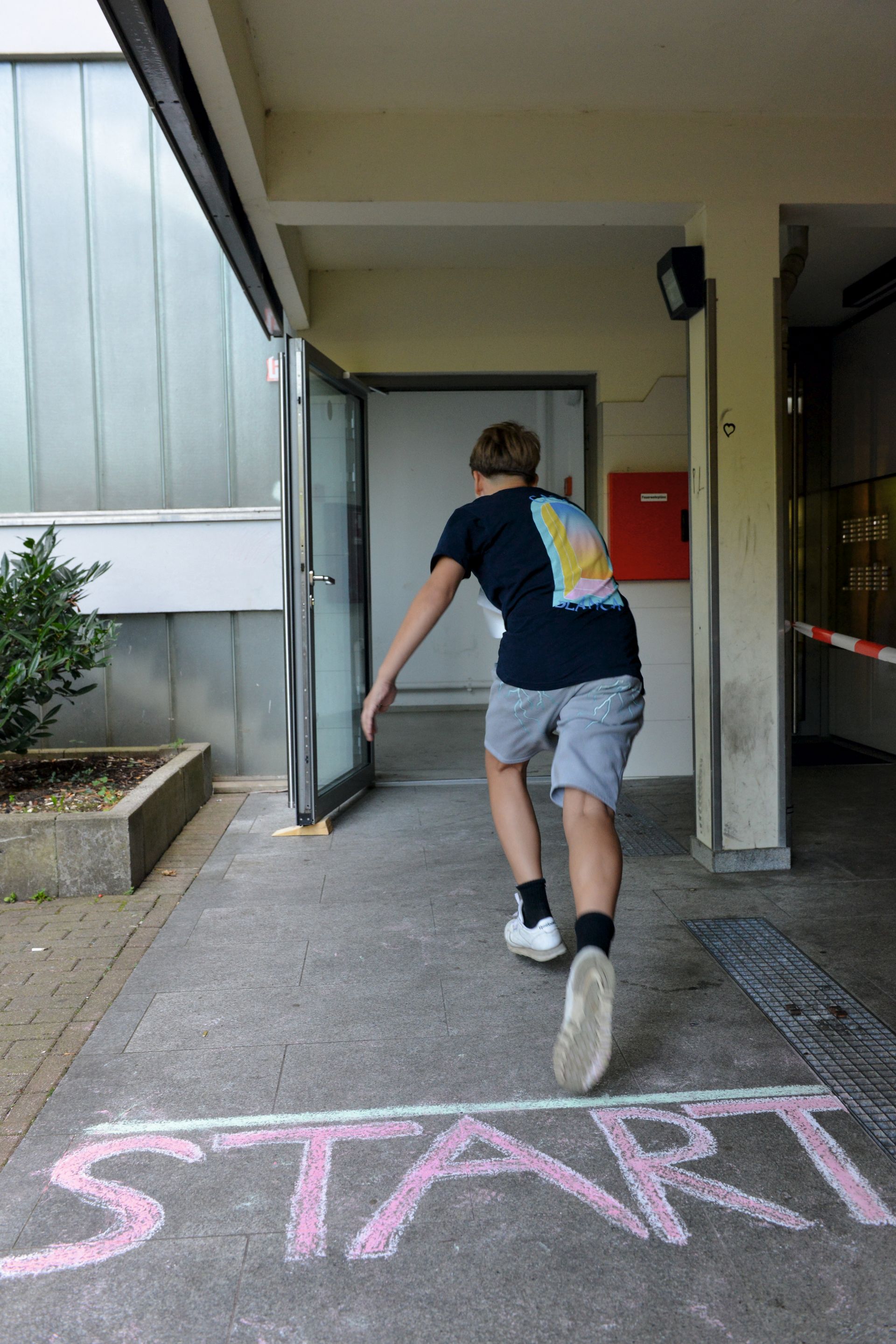 Auf dem Boden steht "Start" ein Junge rennt grade los in einen Hauseingang.