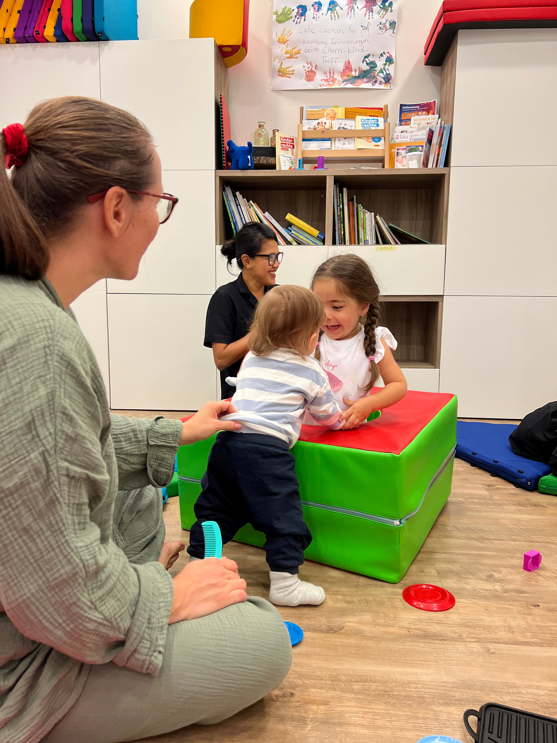 Zwei Kleinkinder die zusammen spielen. Mütter sind im Hintergrund