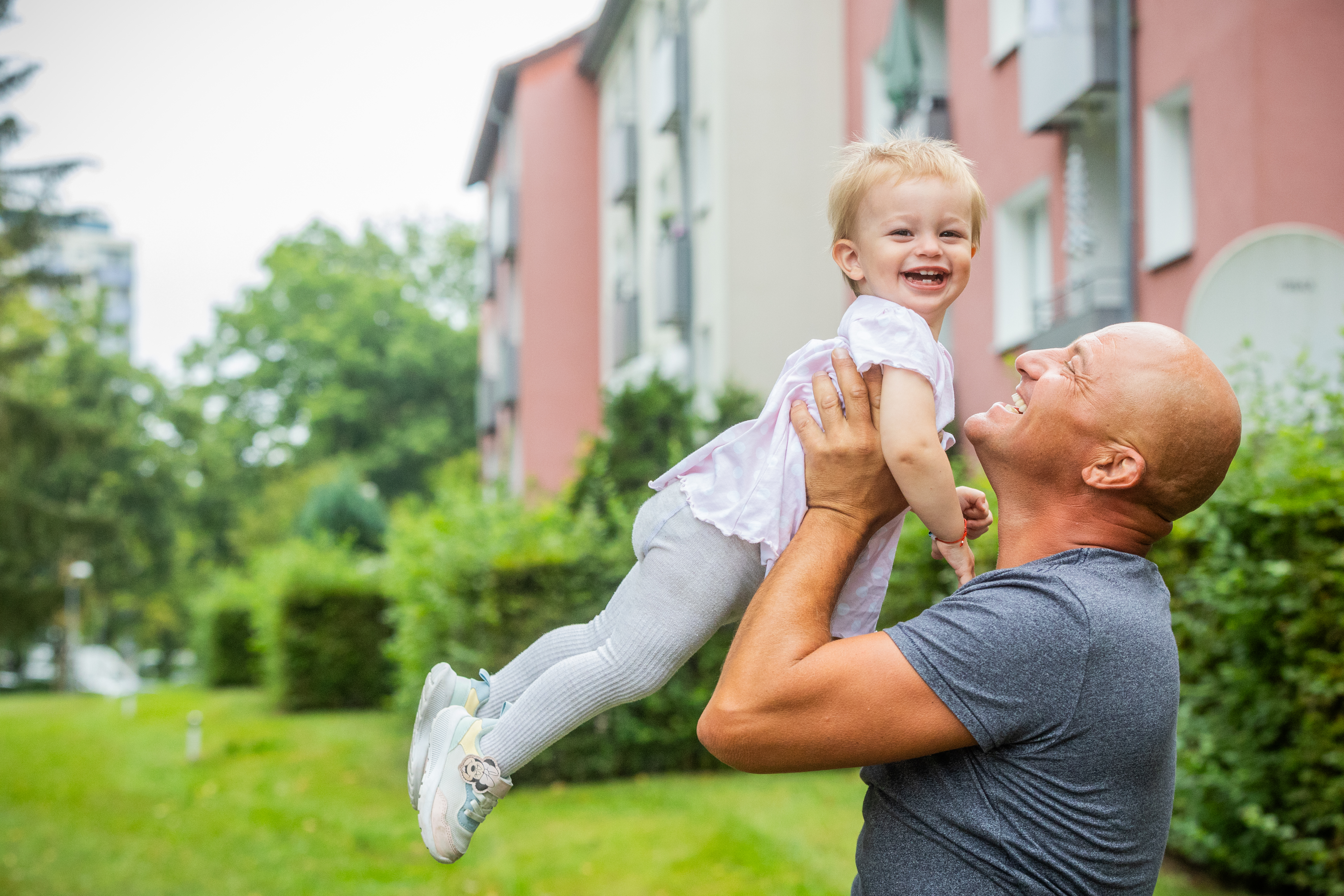Mann und kleinen Kind sind vor einem Haus. Der Mann hat das Kind auf dem Arm.